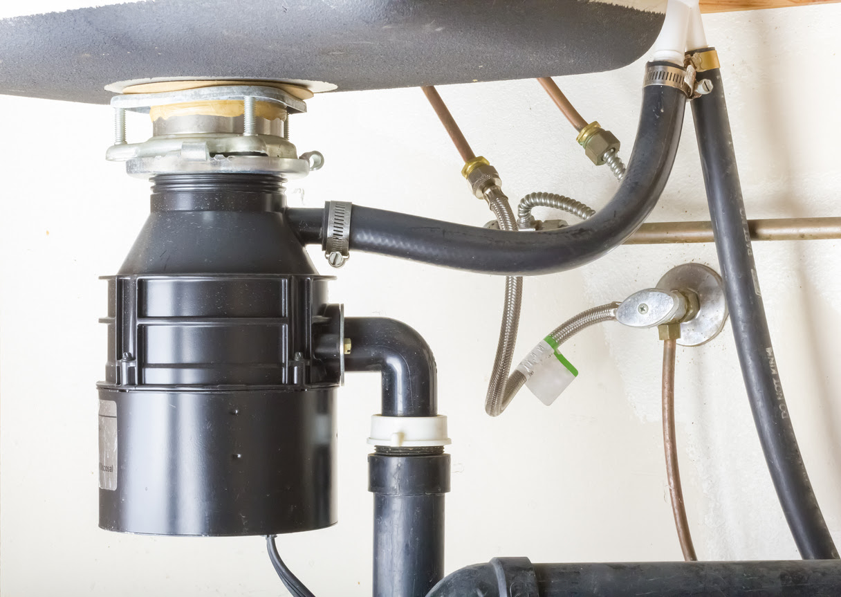 A black garbage disposal unit connected under the sink in the kitchen.